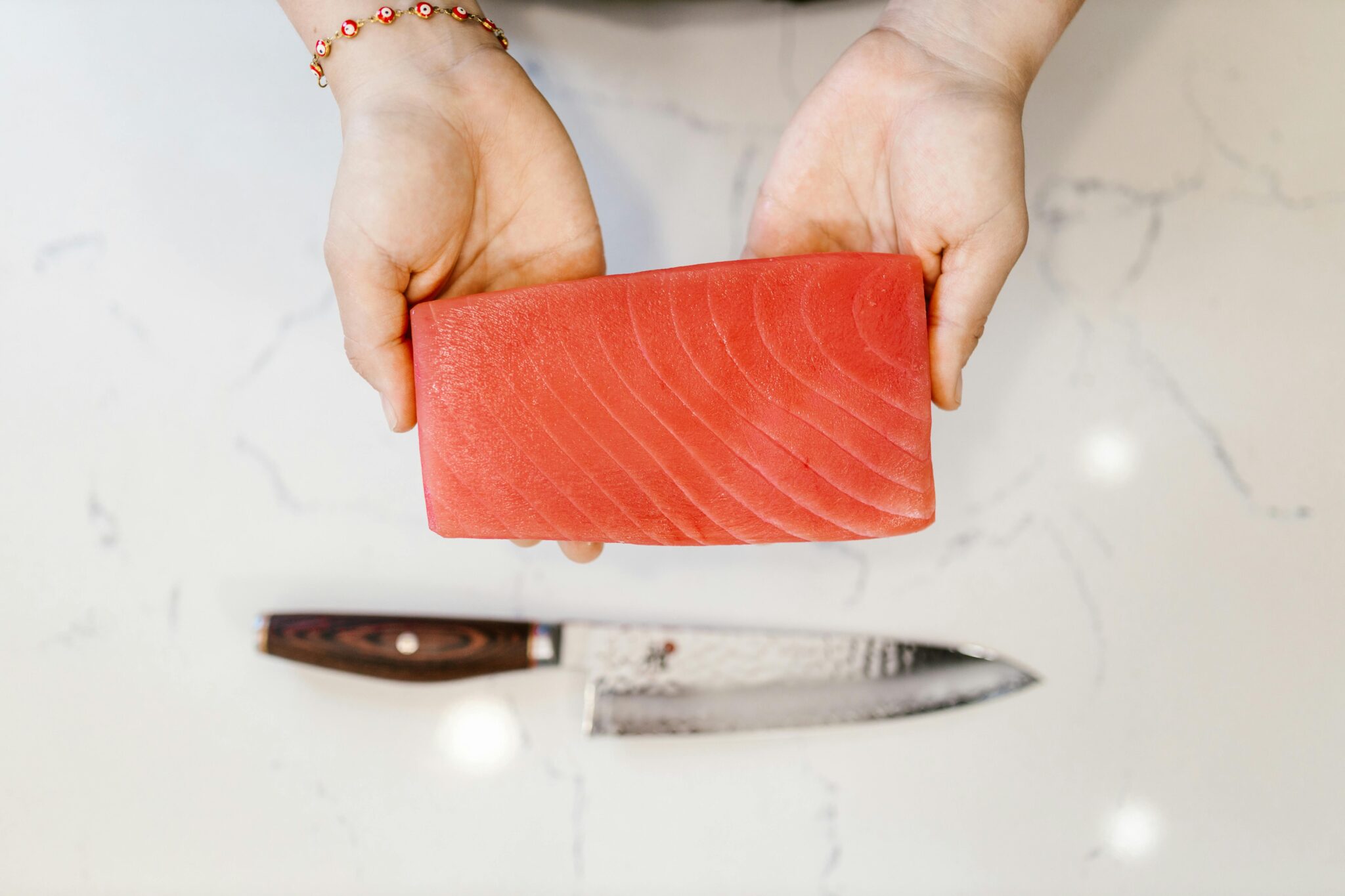Close-up of hands holding a fresh tuna fillet with a knife on a marble countertop, highlighting seafood preparation.